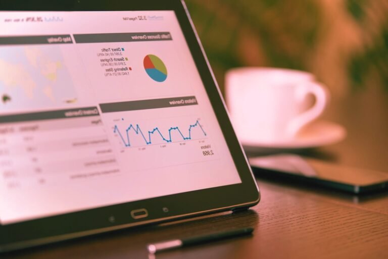 A tablet screen displaying business analytics charts and data graphs on a wooden office desk, symbolizing software development, tech jobs, and recruitment.